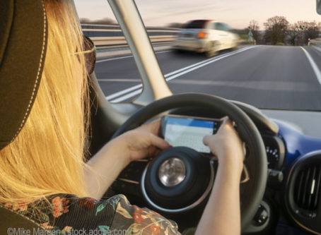 Distracted driving - Woman driving the car while texting message on a smartphone