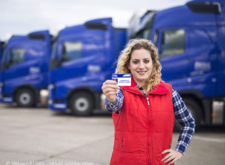 CDL training, Woman truck driver proudly holding commercial driving license.