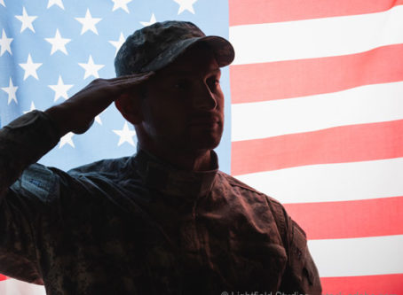 Patriotic military man in uniform and cap giving salute near American flag